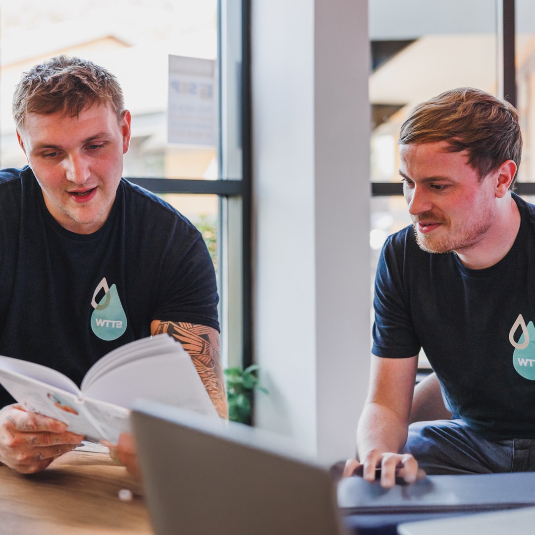 Two men reading a book and discussing with a laptop in the foreground