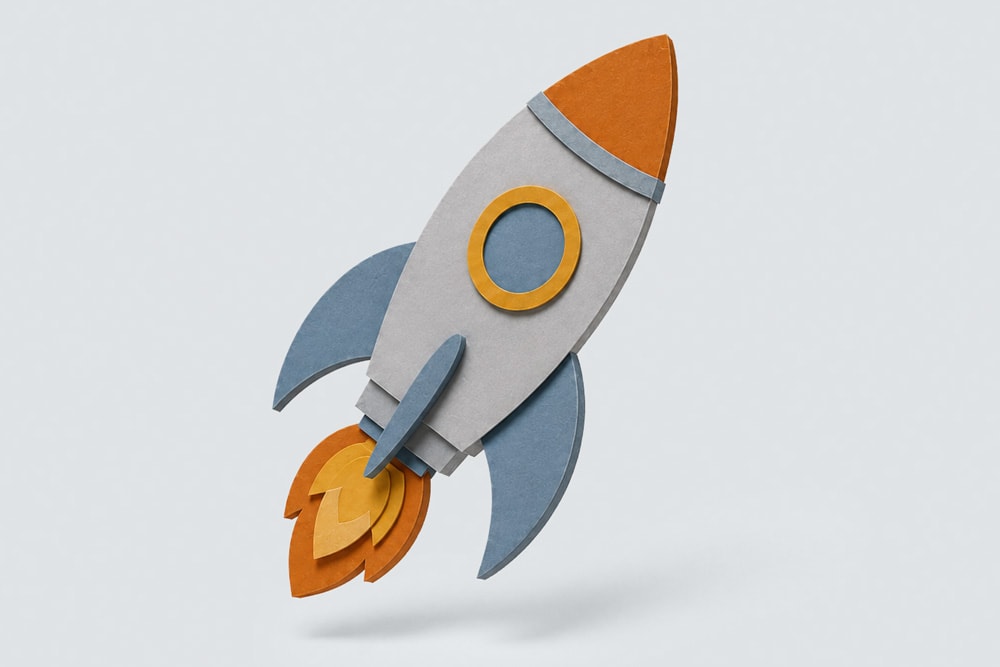 Paper rocket ship with orange and blue details, appearing to launch with flames at the base.