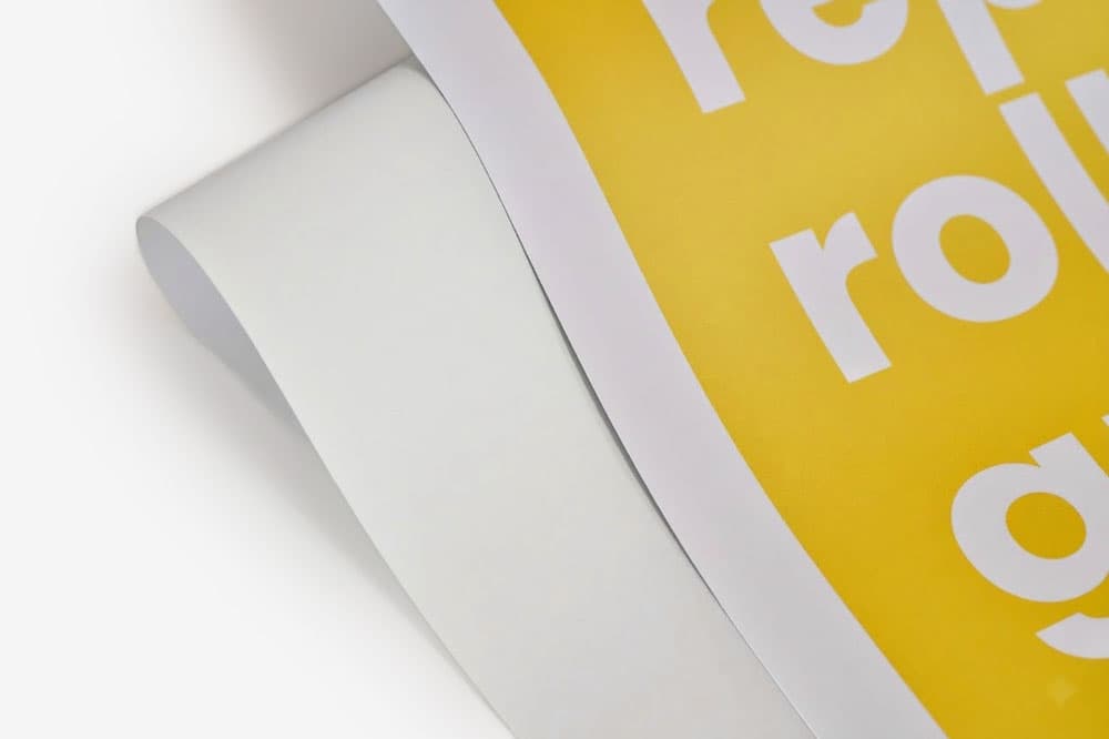 Close-up of a curled yellow poster with white text on a white surface.