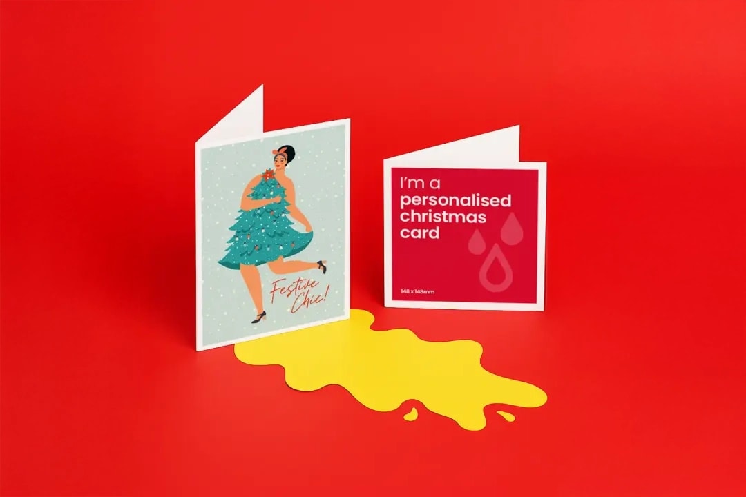 Two Christmas cards stand upright on a red surface with a yellow puddle beneath them.