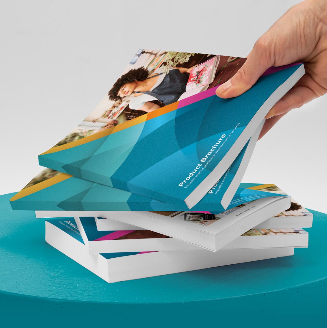 A hand gripping a stack of product brochures resting on a blue table, showcasing various book designs and information.