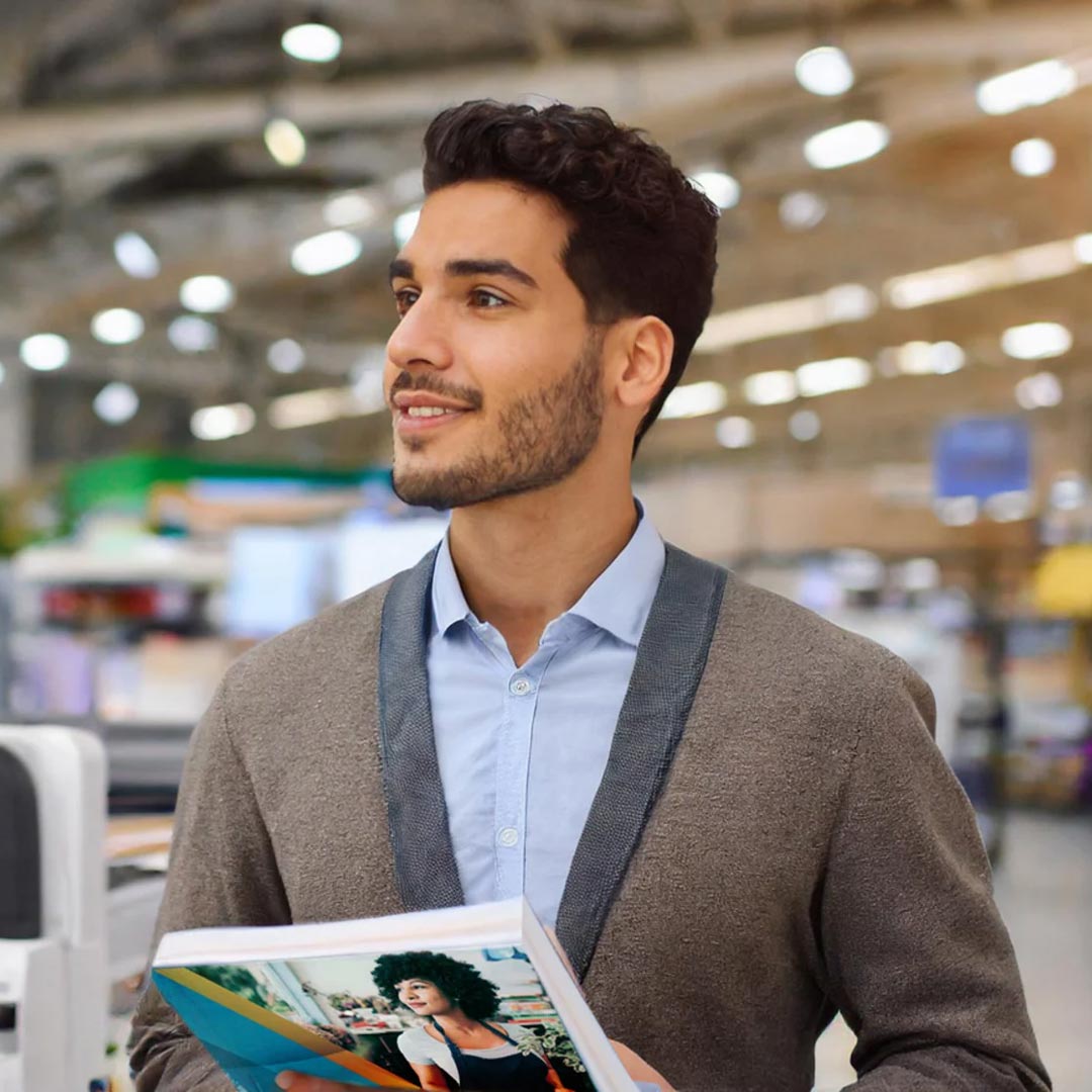 A man holds a product catalogue while standing in a retail store aisle.
