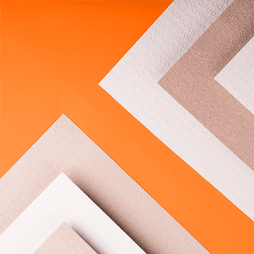 A stack of different specialty papers atop a bright orange surface