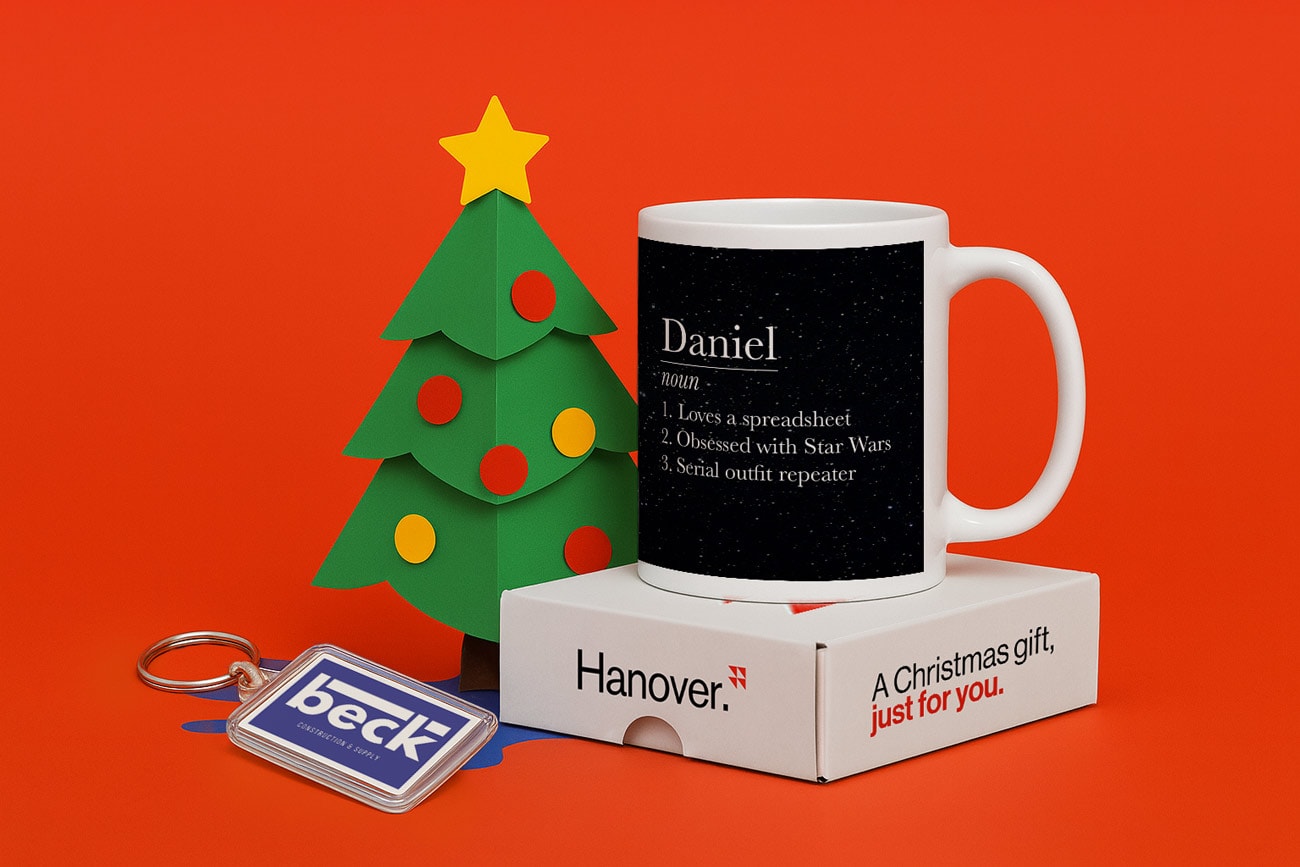 White mug with personalised text on a box next to a paper Christmas tree and a logo keychain.