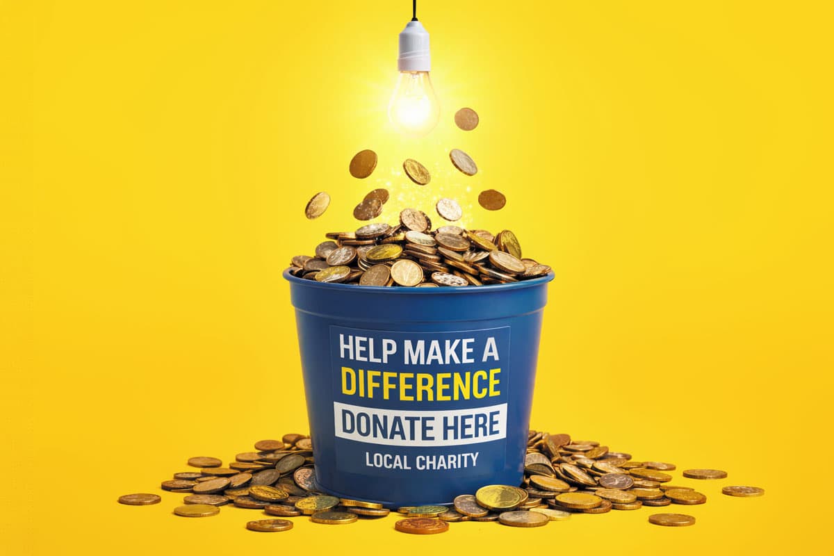 Blue donation bucket filled with coins under a glowing light bulb, yellow background.